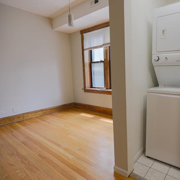 a white dryer is in a room with wood floors and a window.