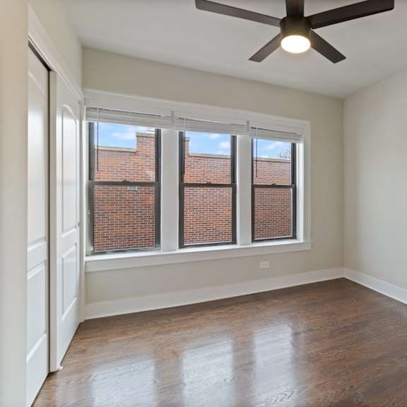 a room with a ceiling fan and a window with a view of a brick building.
