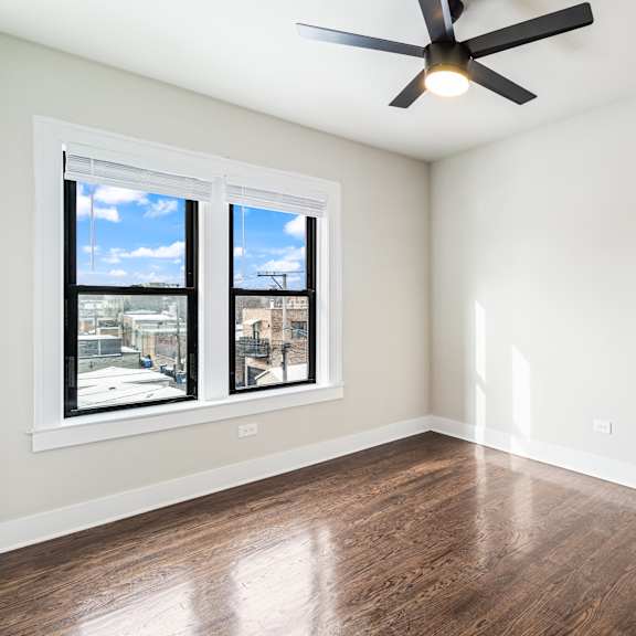 a room with a ceiling fan and two windows.