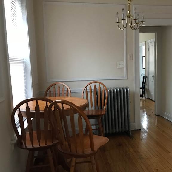 a room with a chandelier, a table with chairs, and a radiator.
