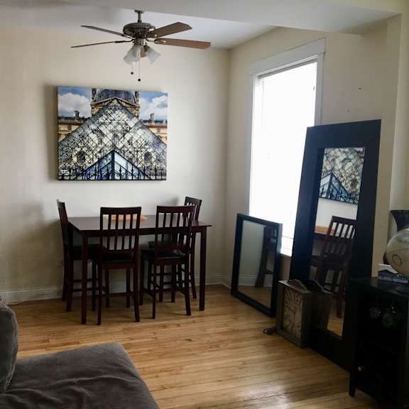 a room with a ceiling fan, a dining table with chairs, and a painting on the wall.