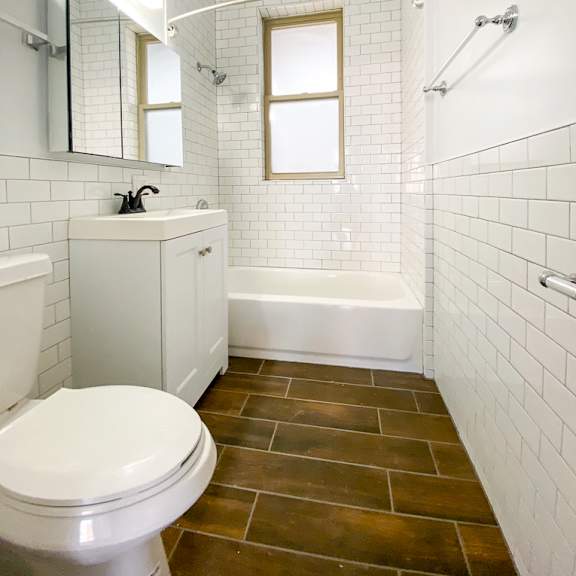 a white toilet sits in a bathroom with a white tub and a window.
