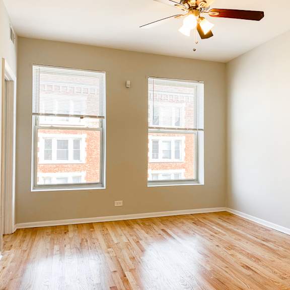 a room with a ceiling fan and two windows.