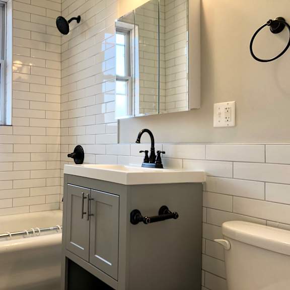 a bathroom with a white tub, sink, and grey cabinet.