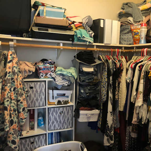 a cluttered closet with clothes and a computer monitor on the shelf.