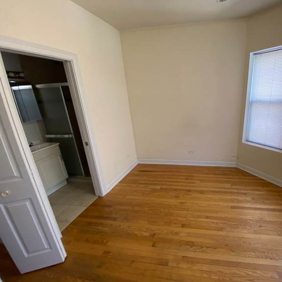 a room with wooden floors and a white door leading to a kitchen.