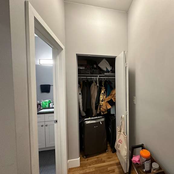 a room with a doorway leading to a closet with clothes hanging and a suitcase on the floor.