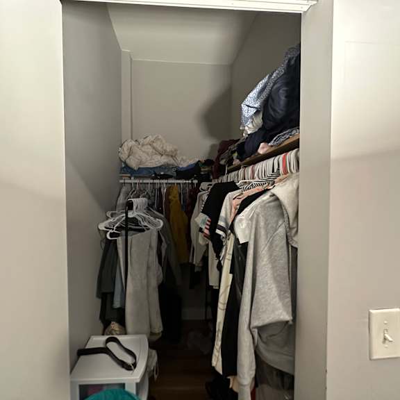 a small closet with clothes hanging on hangers.