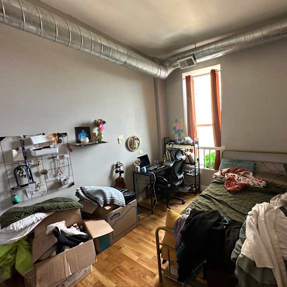a room with a bed, desk, and clutter.
