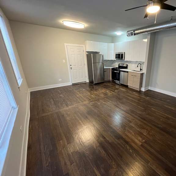 a room with wooden flooring and a kitchen area in the background.