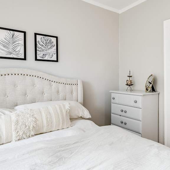 a white bedroom with a large bed, a dresser, and a mirror.