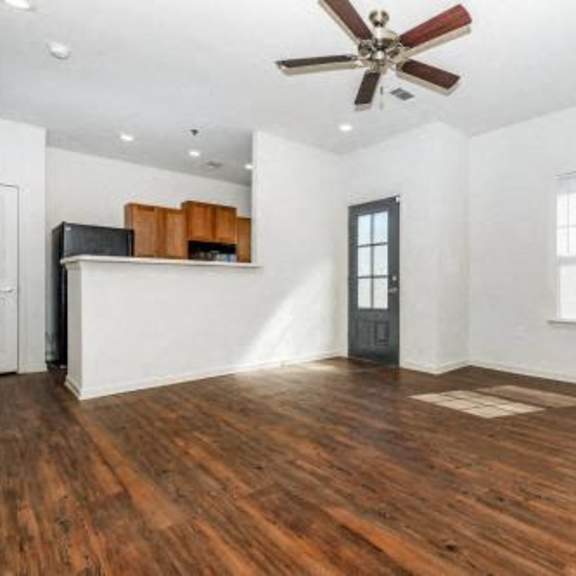 an empty living room with a ceiling fan and a kitchen