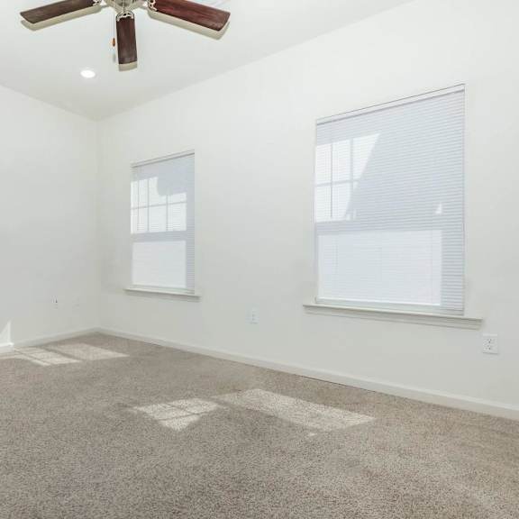 an empty living room with a ceiling fan and two windows