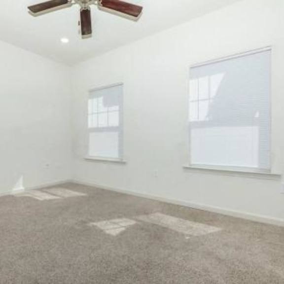 an empty living room with a ceiling fan and two windows