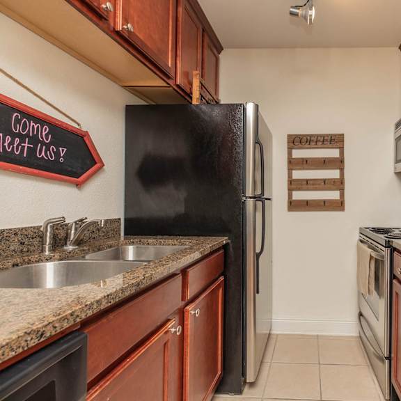 a kitchen with a black fridge and wooden cabinets. at the cove at state street apartments, baton rouge, la