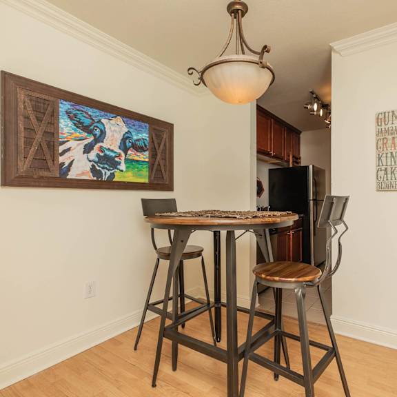 a dining room with a table and chairs and a painting on the wall. at the cove at state street apartments, baton rouge