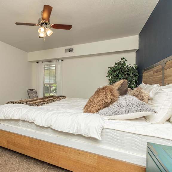 a bedroom with a bed, pillows, a ceiling fan, and a window with blinds. at the cove at state street apartments, baton rouge, la