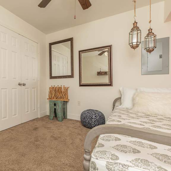 a bedroom with a bed, a mirror, a ceiling fan, and a wall-mounted light fixture. at the cove at state street apartments, baton rouge, louisiana