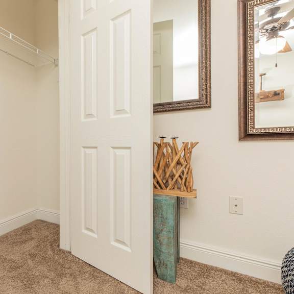 a white door is in a room with a mirror and a vase on the wall. at the cove at state street apartments, baton rouge, la