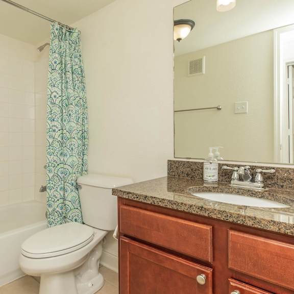 a white toilet sits next to a bathtub in a bathroom. at the cove at state street apartments, louisiana