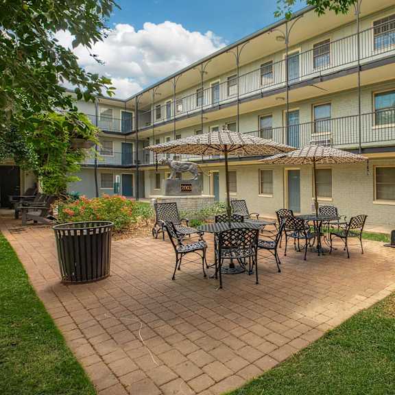 a patio with a table and chairs is surrounded by a grassy area and a building. at the cove at state street apartments, louisiana