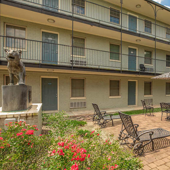 a courtyard with a statue of a lion and chairs and tables. at the cove at state street apartments, baton rouge, la