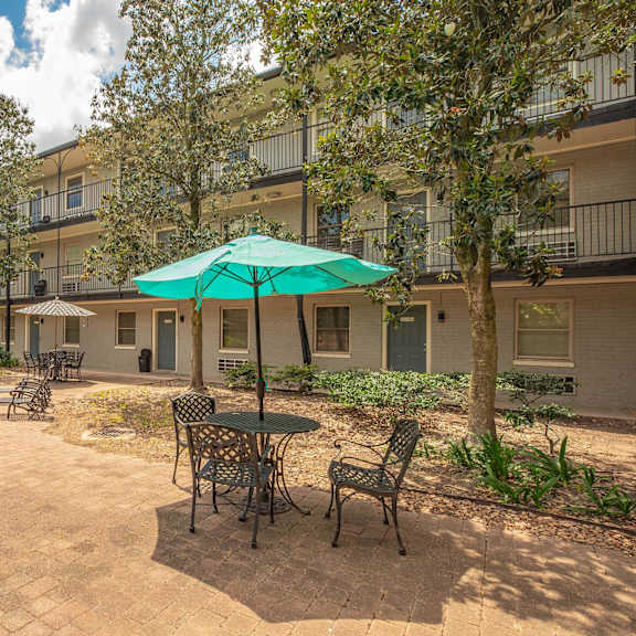 a patio with a table and chairs and a green umbrella. at the cove at state street apartments, baton rouge, la