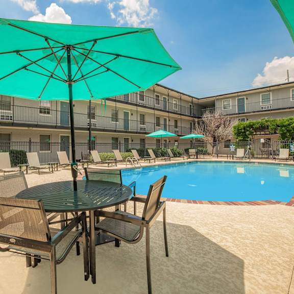 a table with chairs and umbrellas is set up by a pool. at the cove at state street apartments, louisiana, 70802