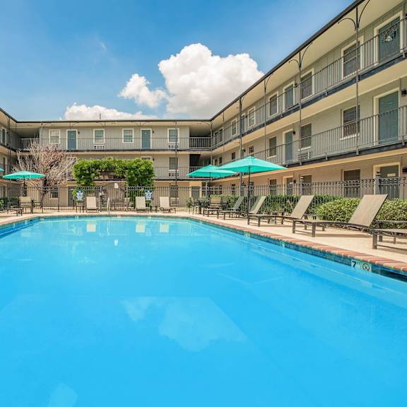 a large swimming pool in a resort with sun loungers and umbrellas. at the cove at state street apartments, baton rouge, la