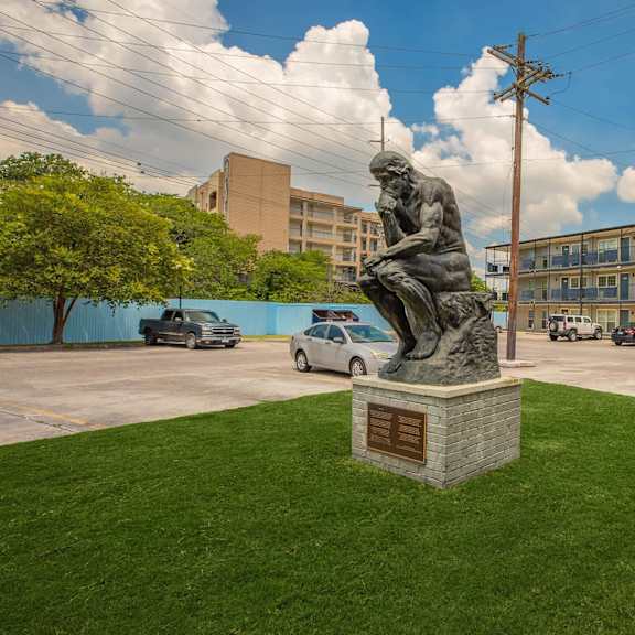 a statue of a man reading is in the middle of a grassy area. at the cove at state street apartments, baton rouge, la