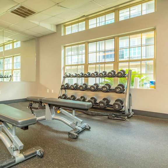 a gym with a bench, weights, and windows. at the cove at state street apartments, louisiana, 70802