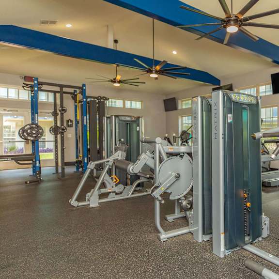 a gym with a variety of equipment including a weight machine and a bench press. at the cove at state street apartments, baton rouge, la