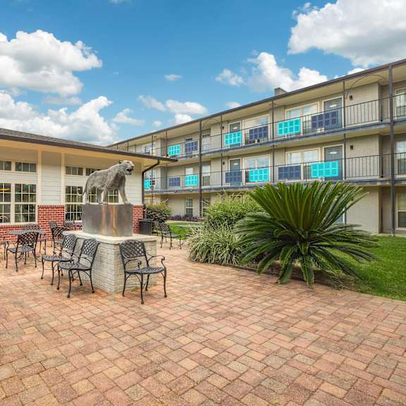a patio with a table and chairs is surrounded by plants and a brick building. at the cove at state street apartments, louisiana