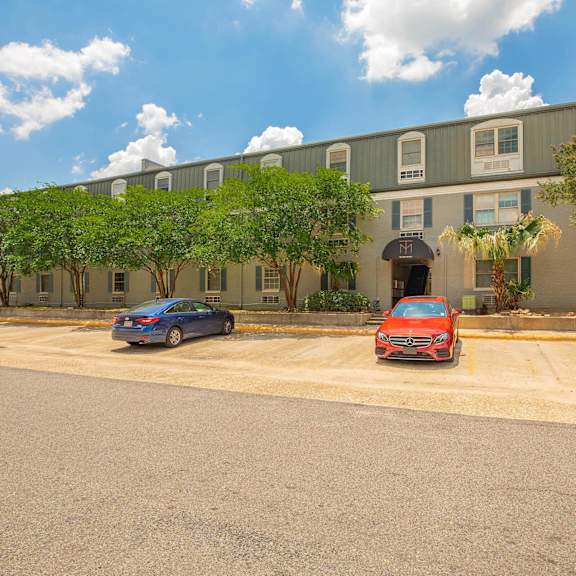 a red car is parked in a parking lot in front of a building. at the cove at state street apartments, baton rouge, la