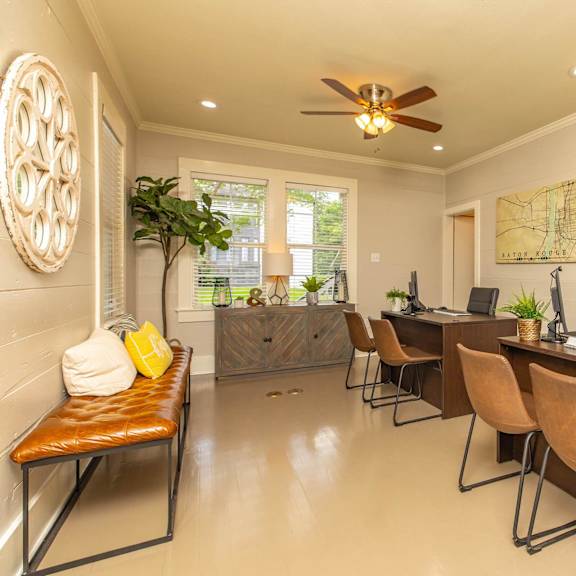 a room with a brown desk and chairs, a ceiling fan, and a map on the wall. at the cove at state street apartments, baton rouge
