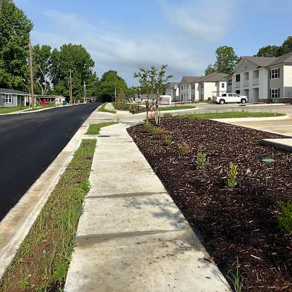 a sidewalk runs parallel to a street with a row of houses on the right.