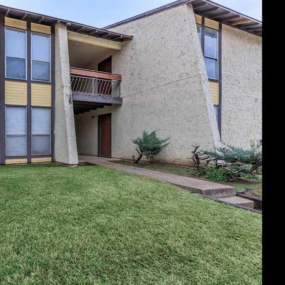 a building with a balcony and a green lawn in front.