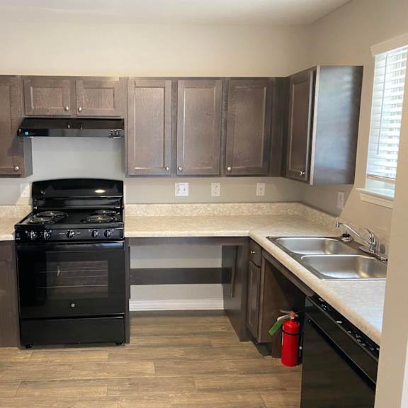 a black fridge and oven in a kitchen with wooden floors and brown cabinets.