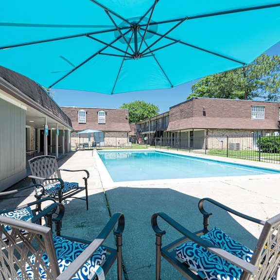 a pool area with chairs and a blue umbrella.