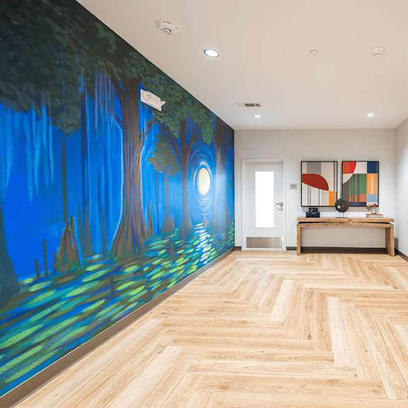 a hallway with a mural of a forest on the wall and wooden flooring.