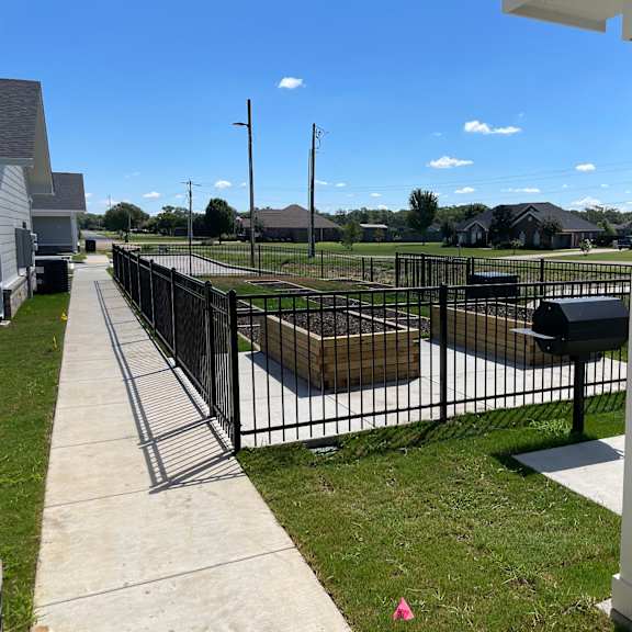 a black fence surrounds a grassy area with a white pillar on the right.