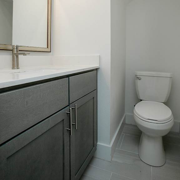 a white toilet sits in a bathroom next to a vanity with a mirror.
