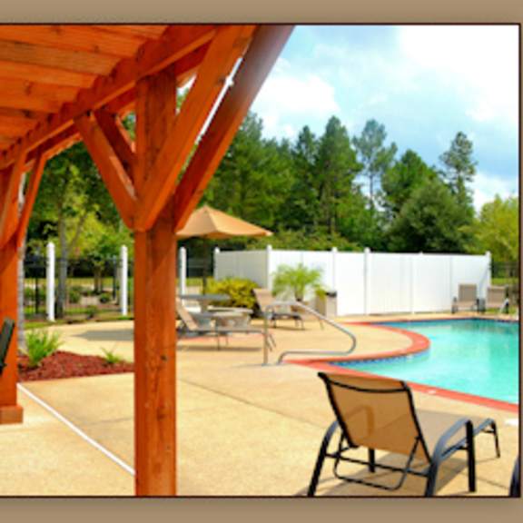 a pool area with a wooden pergola and chairs.