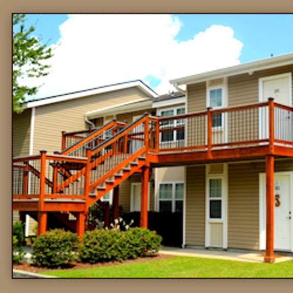 a tan and white two story apartment building with a red staircase.