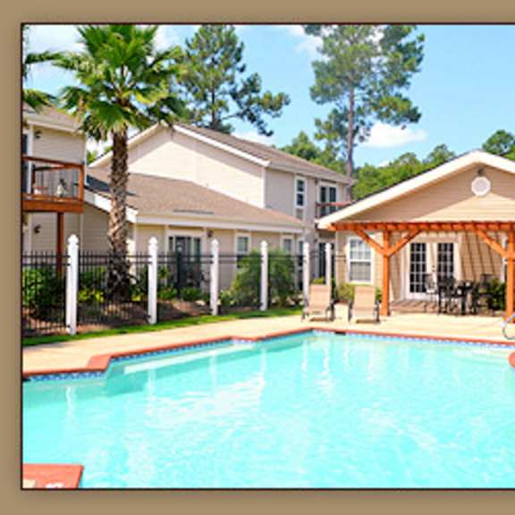 a pool in front of a house with a patio.