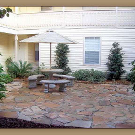 a patio with a table and chairs is surrounded by plants.