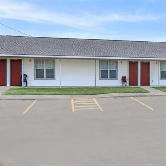 a white building with red doors and windows is surrounded by a parking lot.