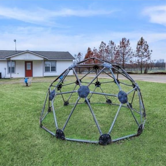 a large metal sculpture in the shape of a sphere is placed on a grassy area.