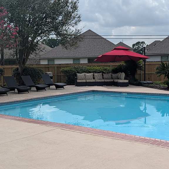 a pool with a red umbrella and black chairs.