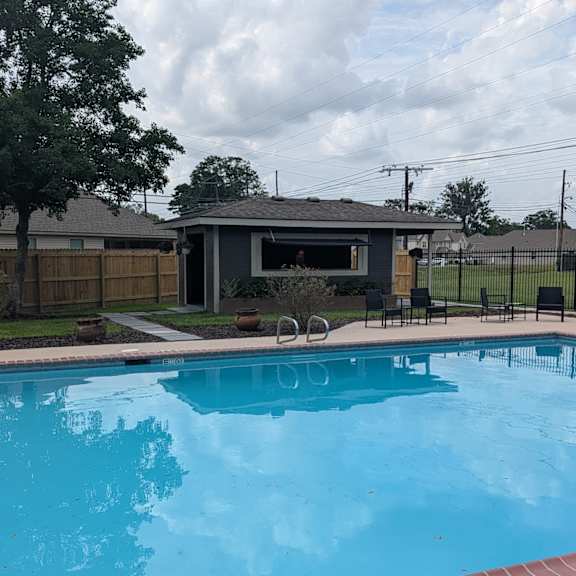 a pool with a red brick border and a house in the background.
